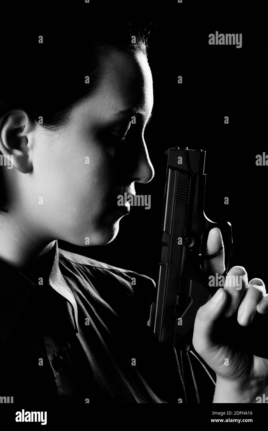 female portrait with gun closeup on black background side view, monochrome Stock Photo