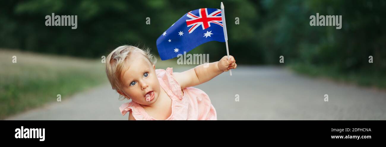 Cute Caucasian baby girl waving Australian flag. Funny child crawling in park celebrating Australia Day holiday. Celebration of national Australia Day Stock Photo