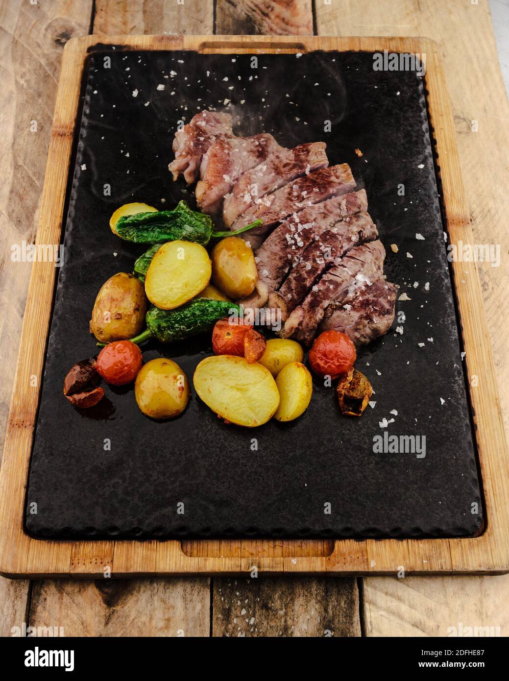 A vertical closeup of grilled meat and vegetables on a nonstick mat on a wooden board Stock Photo