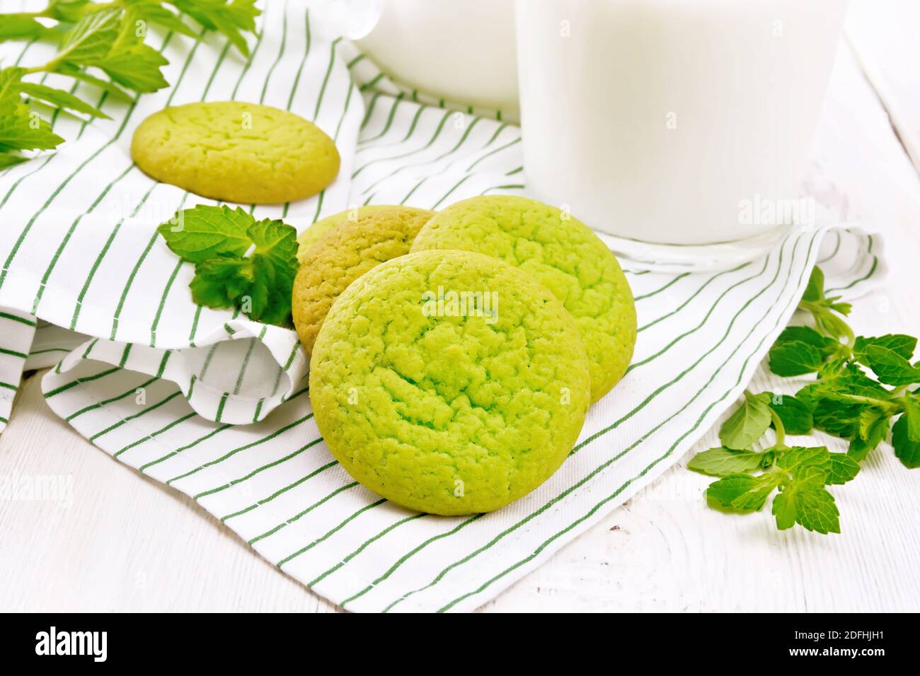 Green mint cookies on a napkin with milk in a glass on the background of light wooden board Stock Photo