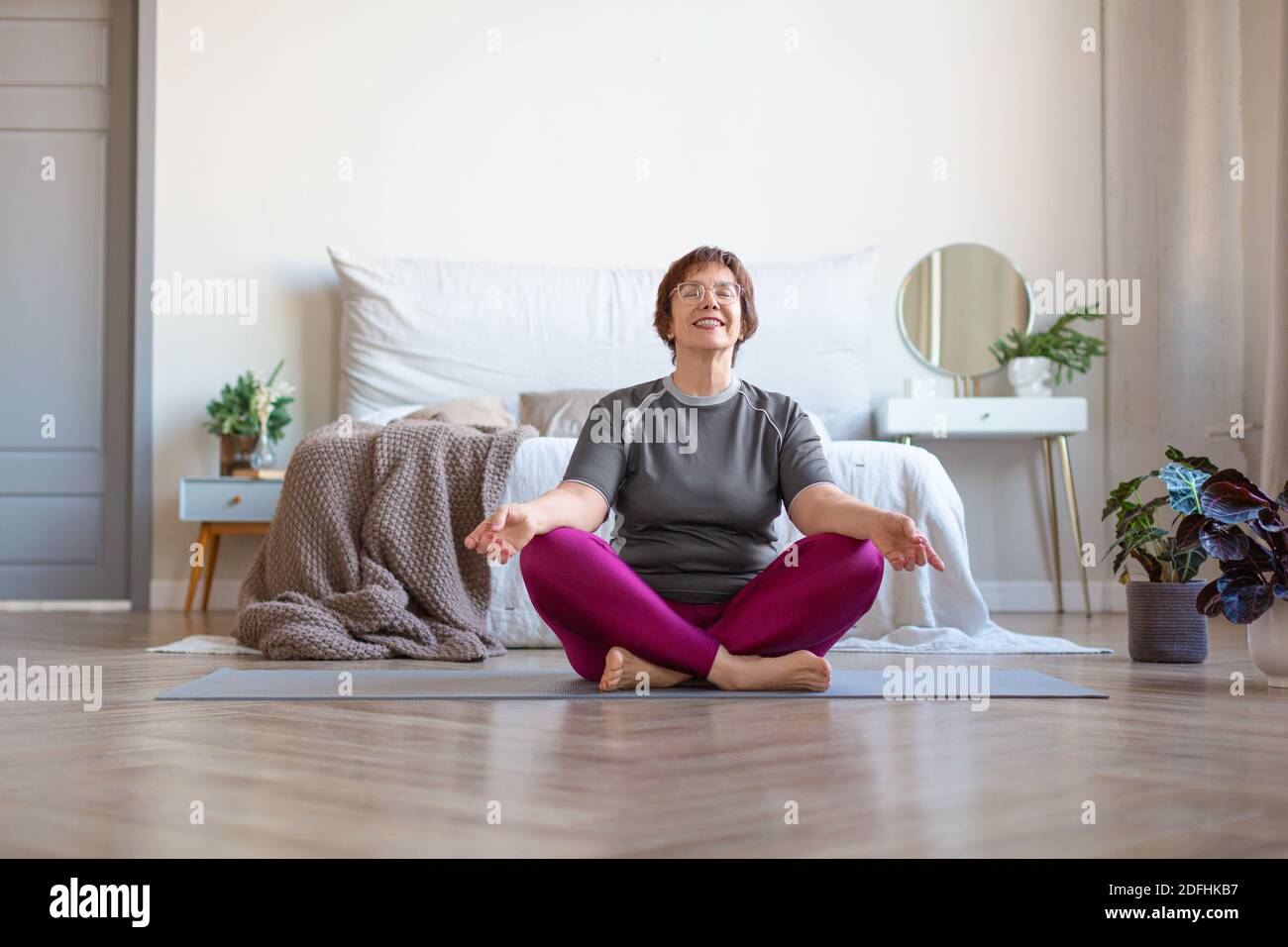 An elderly woman meditates at home in the lotus position. The concept of a healthy and active lifestyle in old age. Stock Photo