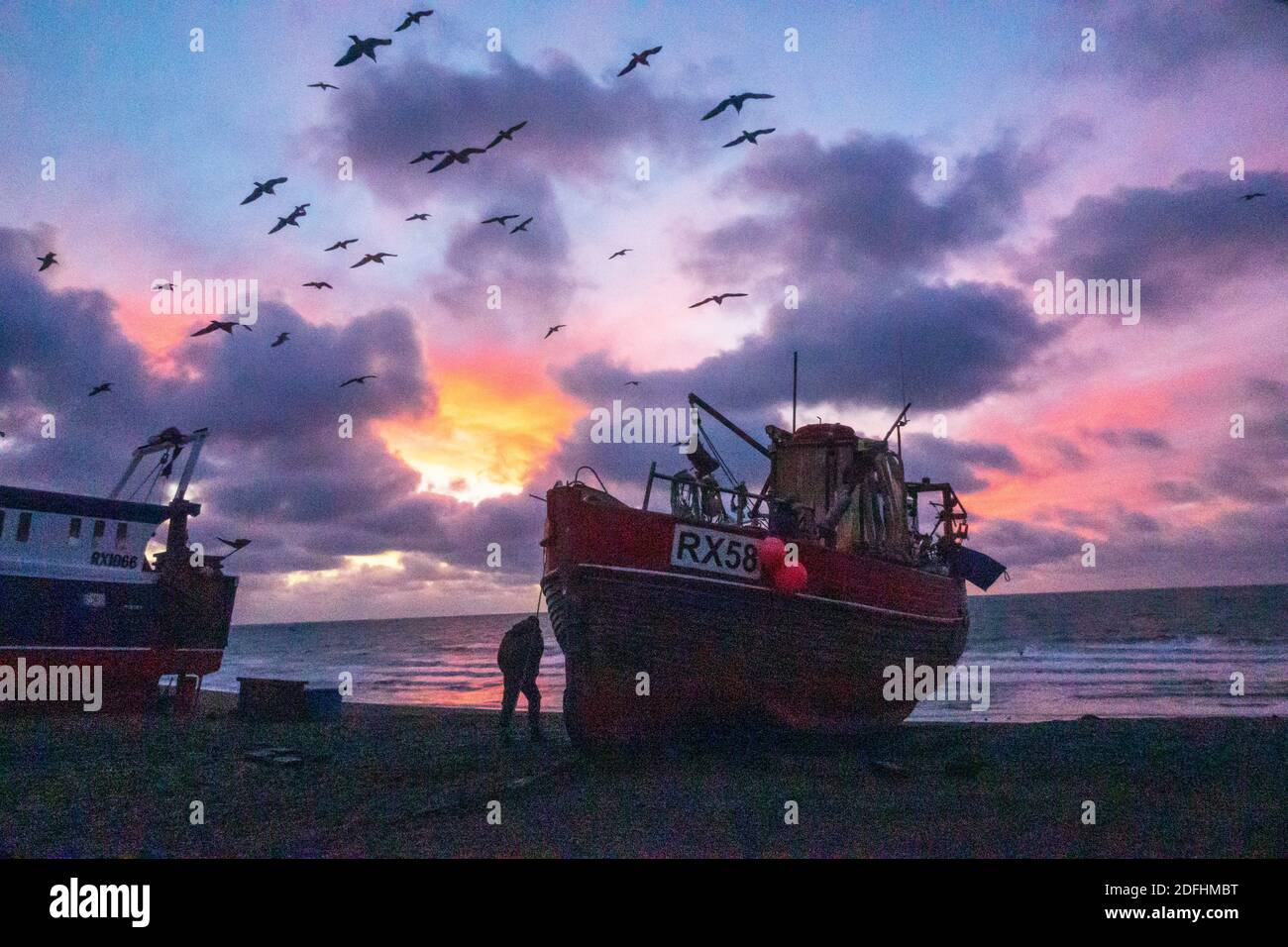 Hastings, East Sussex, UK. 5th December 2020. Seagulls swirl at dawn over Hastings fishing boats with a colourful sunrise over the English Channel, on the day of Boris Johnson's talks with EU President of European Commission, Ursula von der Leyen, to try to break the deadlock over fishing rights in British waters and secure a last minute trade deal. Carolyn Clarke/Alamy Live News. Winter sunrise Stock Photo