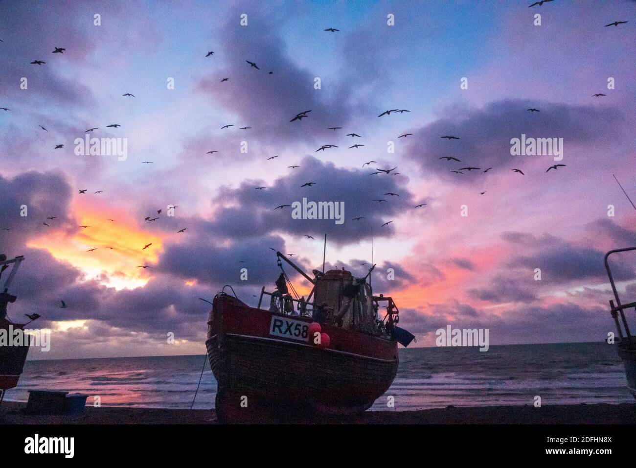 Hastings, East Sussex, UK. 5th December 2020. Seagulls swirl at  dawn over Hastings fishing boats with a colourful sunrise over the English Channel on the day of Boris Johnson's talks with EU President of European Commission, Ursula von der Leyen, to try to break the deadlock over fishing rights in British waters and secure a last minute trade deal. Carolyn Clarke/Alamy Live News. Winter sunrise. Brexit Stock Photo