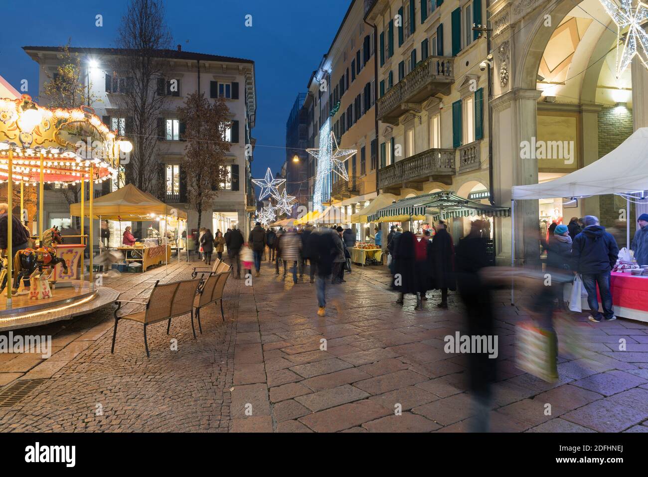 Christmas market in the evening and crowd of people on the street of a city with christmas lights. Historic center of Varese, Corso Matteotti, Italy Stock Photo