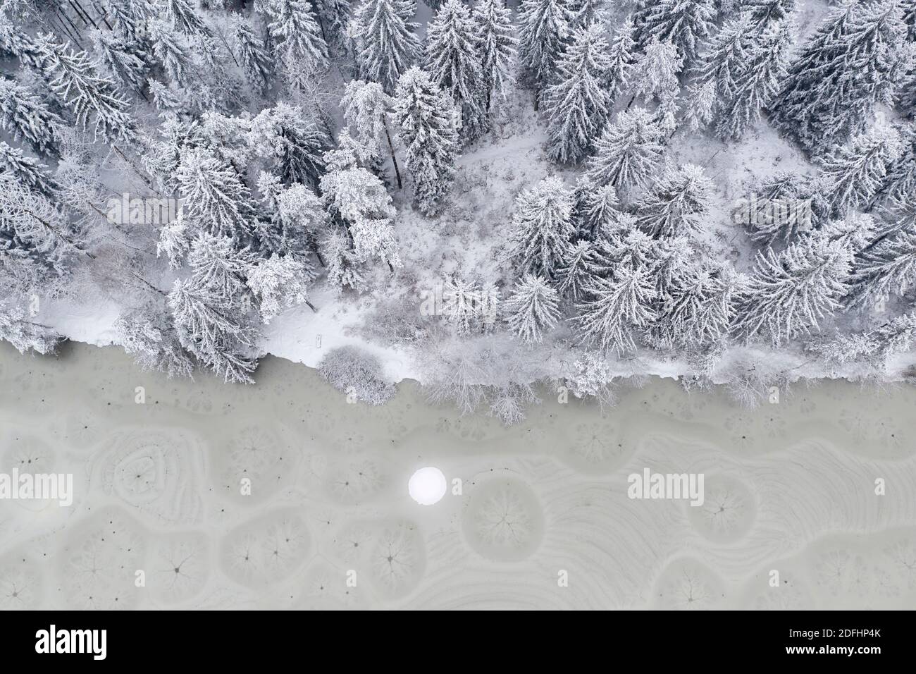 An aerial drone looking down captures patterns, shapes, holes and cracks in frozen lake ice. Stock Photo