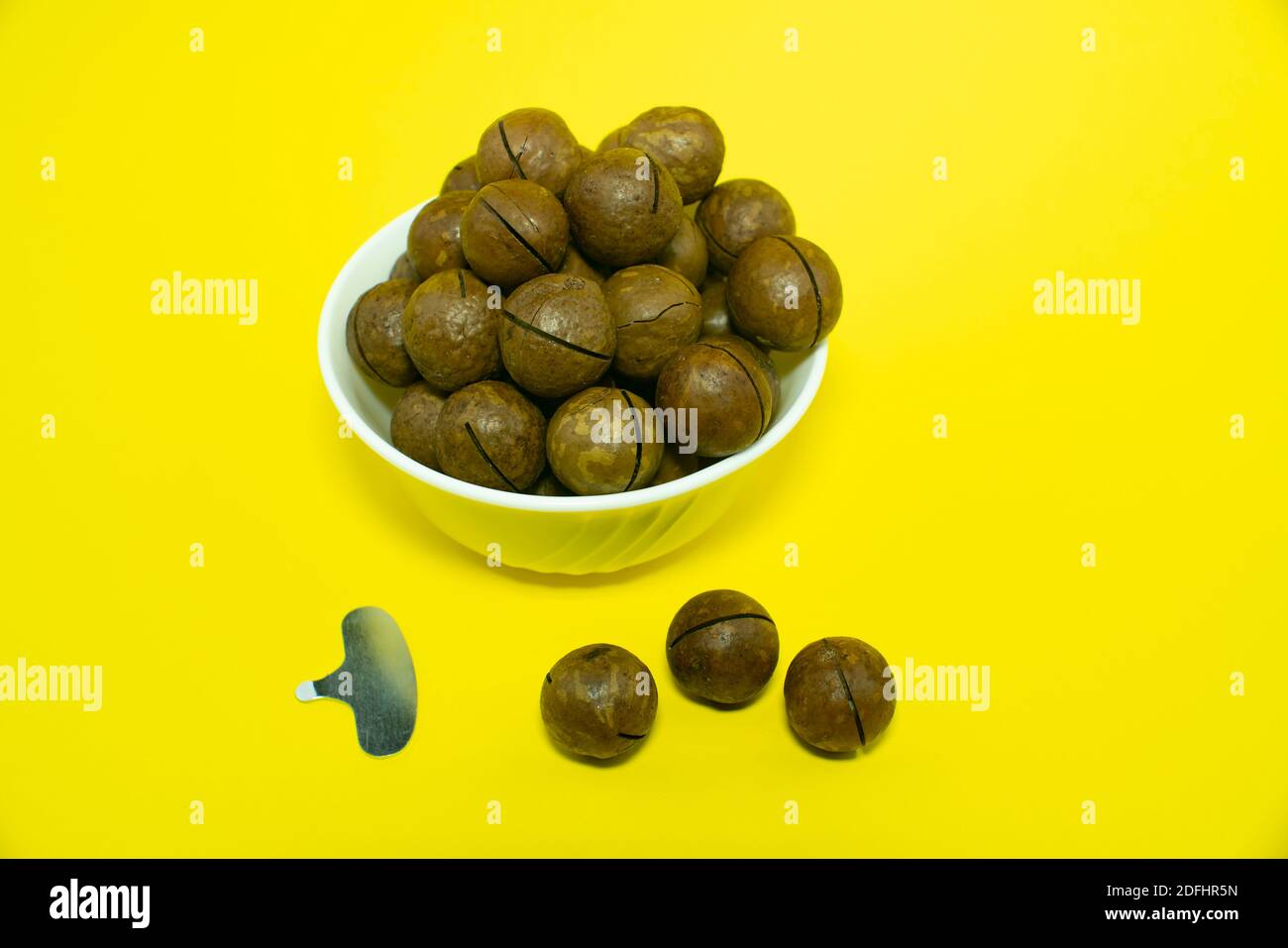Macadam nuts in a white cup. White plate isolated on yellow background. Closed in and around a plate with an opening tool. Stock Photo
