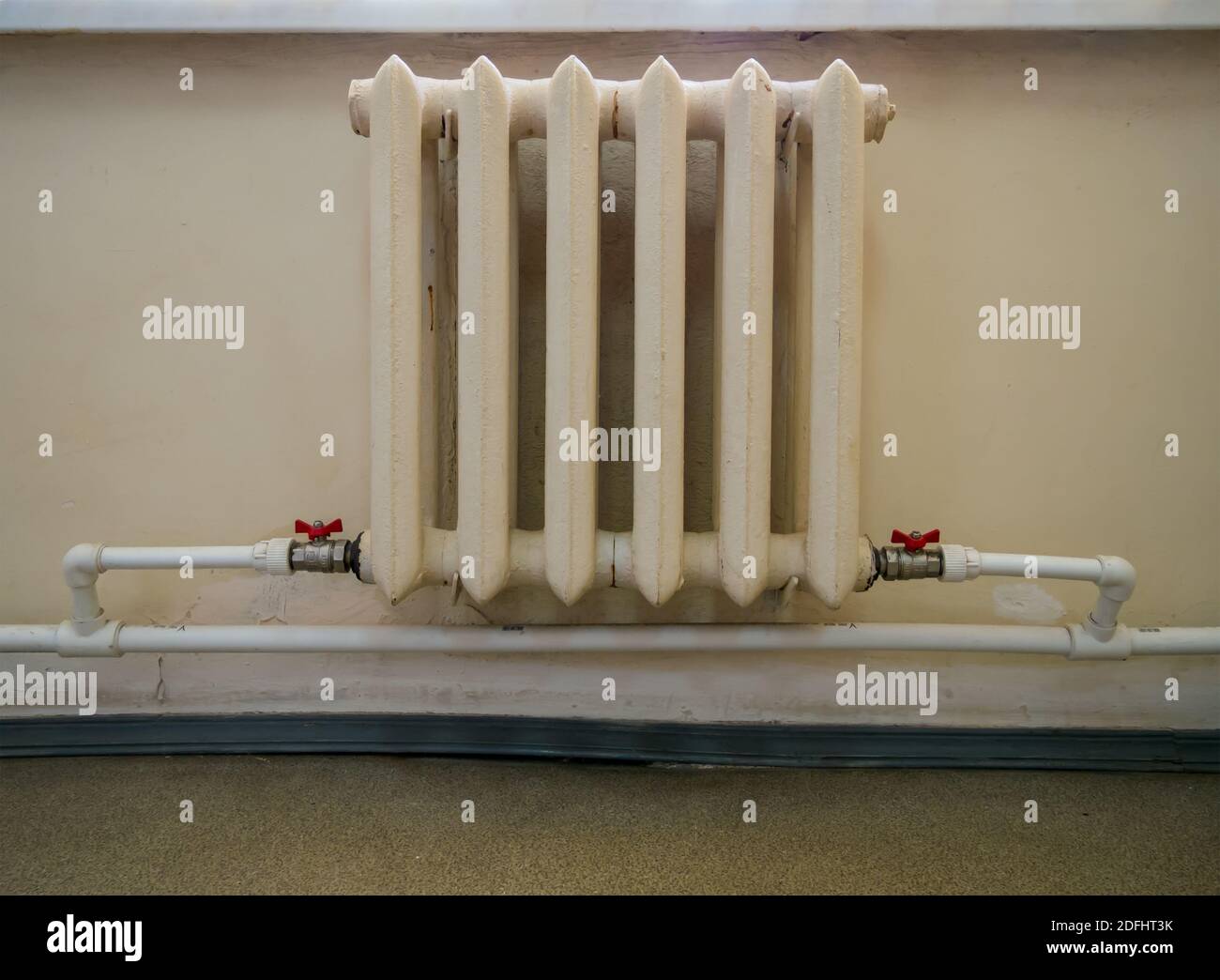 A castiron radiator is connected with plastic pipes to the heating