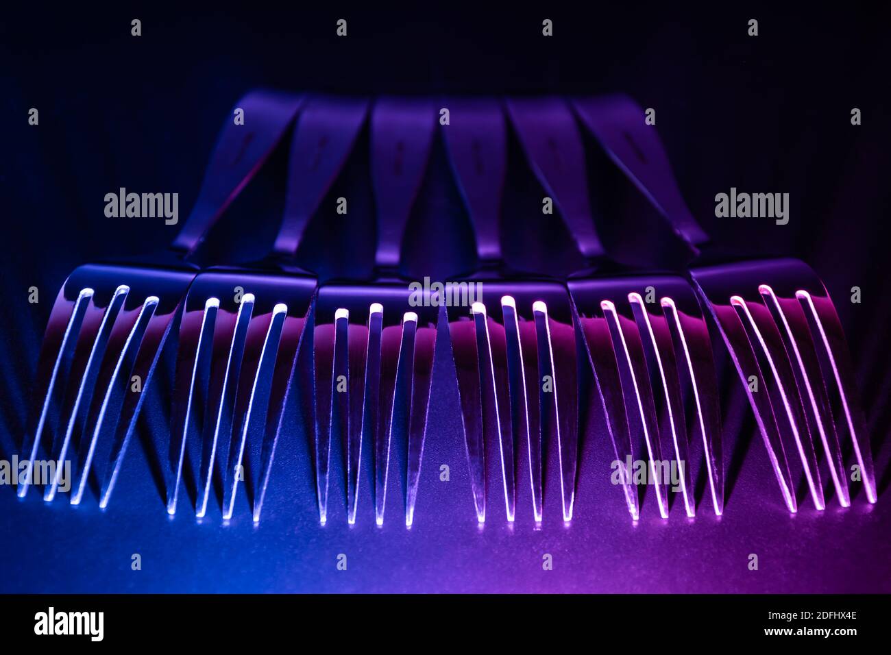 A set of forks in a raw with blue and violet coloured gradient led light in the dark. Stock Photo