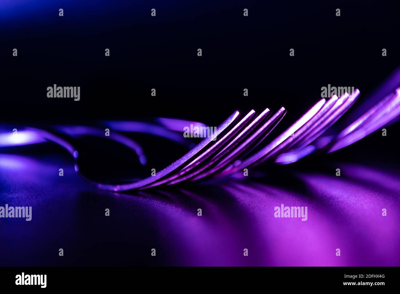 Set of forks in the dark with blue and violet coloured gradient led light.  Stock Photo
