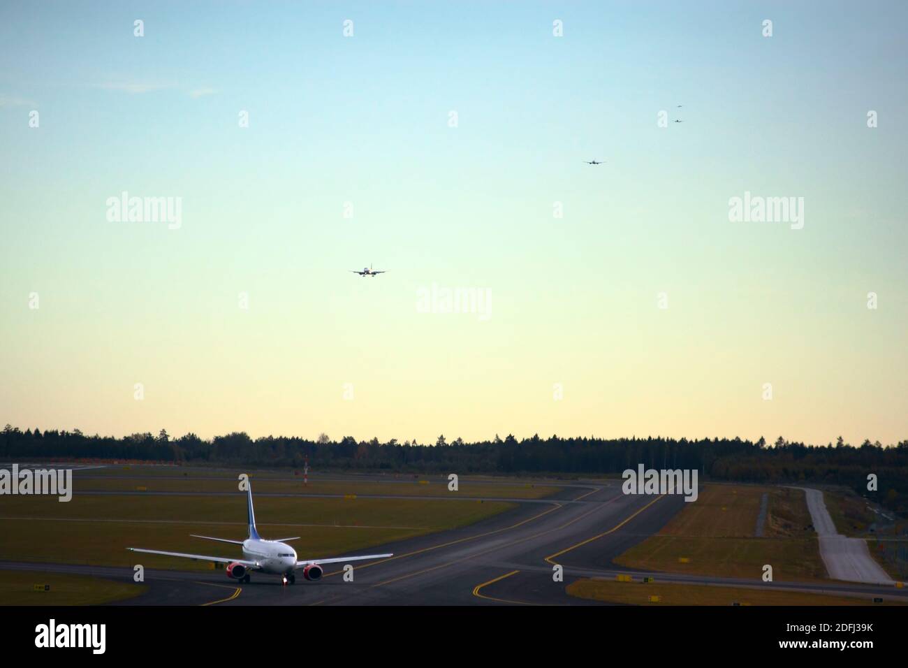 Taxiing airplane and four airplanes in the air in queue to land Stock Photo