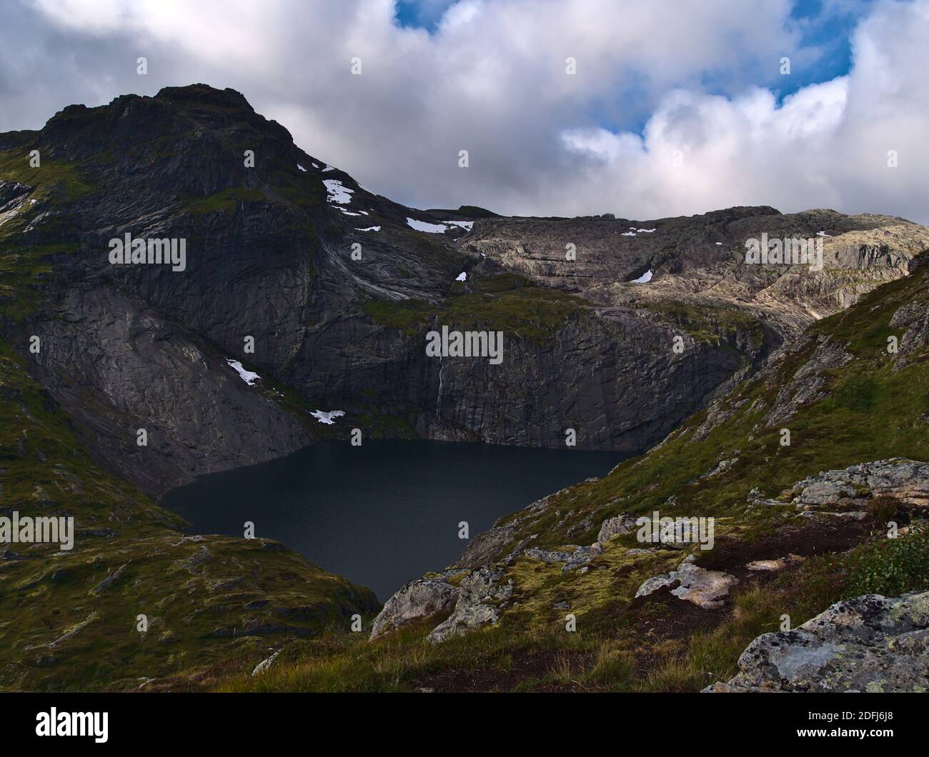 Beautiful view of lake Fjerddalsvatnet surrounded by steep mountains with snow on Moskenesøy island, Lofoten, Norway with hiking path and green meadow. Stock Photo