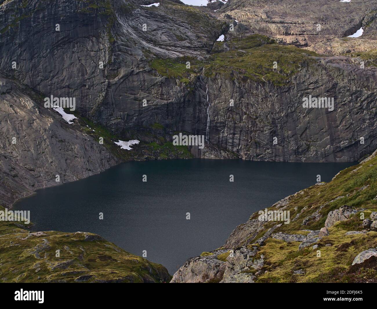 Stunning view of Fjerddalsvatnet lake surrounded by steep mountains with tall waterfall on Moskenesøy island, Lofoten, Norway with snow. Stock Photo
