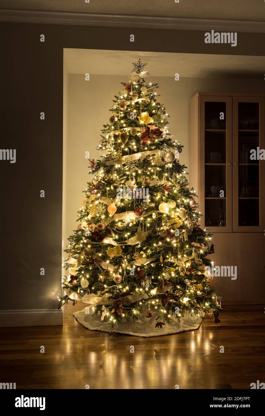 Carefully and beautifully decorated xmas tree in the corner of a modern home with wooden floors Stock Photo