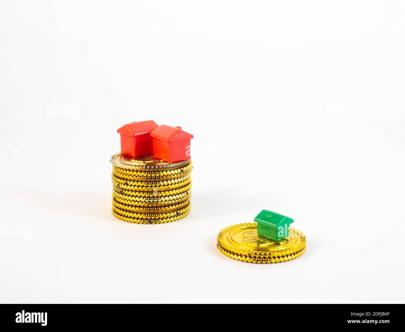 A gradient of a stack of coins, with mini houses in red colors on the larger stack and a green house on the smaller stack. Concept around real estate, Stock Photo