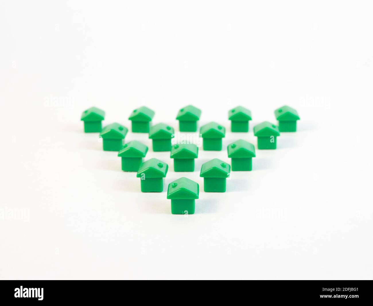Green colored pawns in the shape of a house with gold coins. Concept around housing and real estate agents. Stock Photo