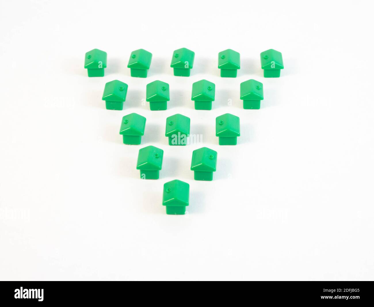 Green colored pawns in the shape of a house with gold coins. Concept around housing and real estate agents. Stock Photo
