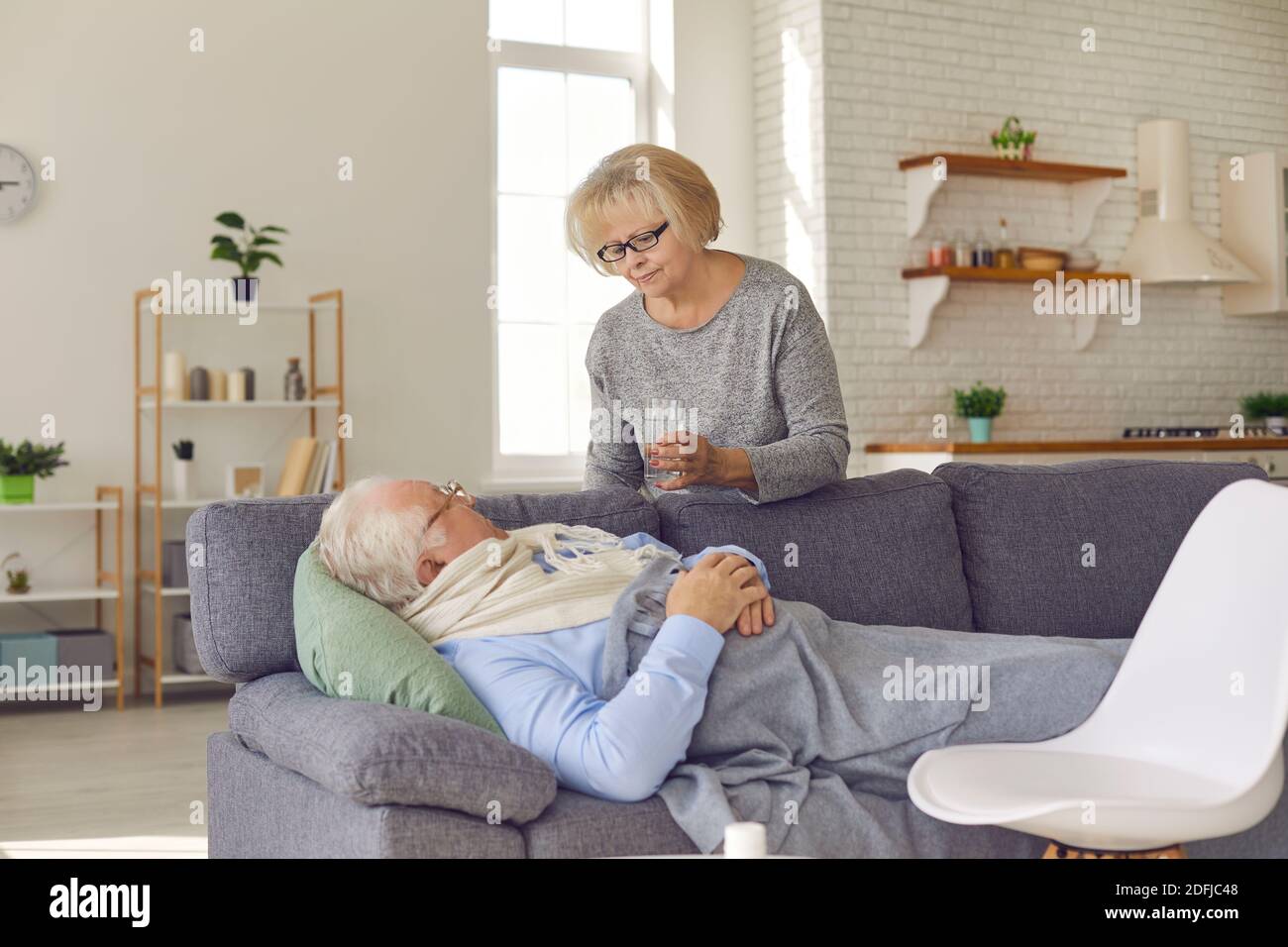 Senior woman grandmother taking care and bringing water to ill husband feeling fever Stock Photo