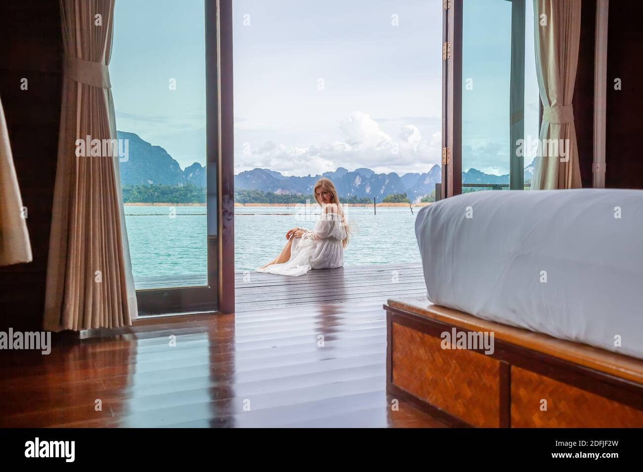 Travel Woman in White Dress Sitting Outdoor near Wooden House on Water ...