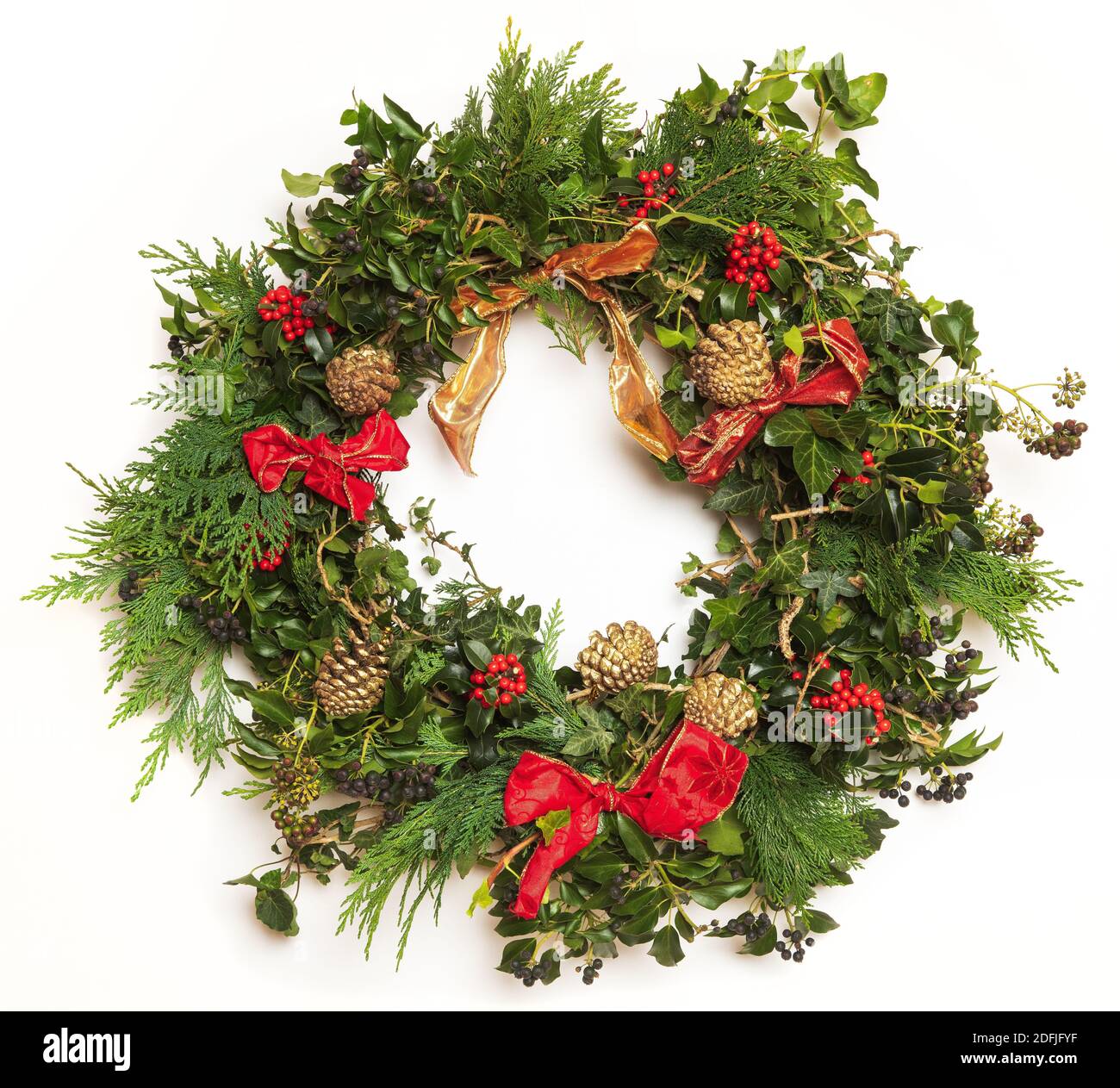 Isolated home made festive Christmas wreath made from ivy, holly, Conifer, Fir cones and ribbons. Stock Photo