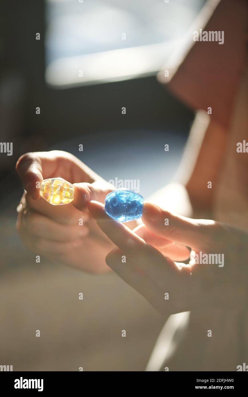 Hands of young female artisan holding blue and yellows handmade glass beads while deciding what color to choose for new necklace Stock Photo