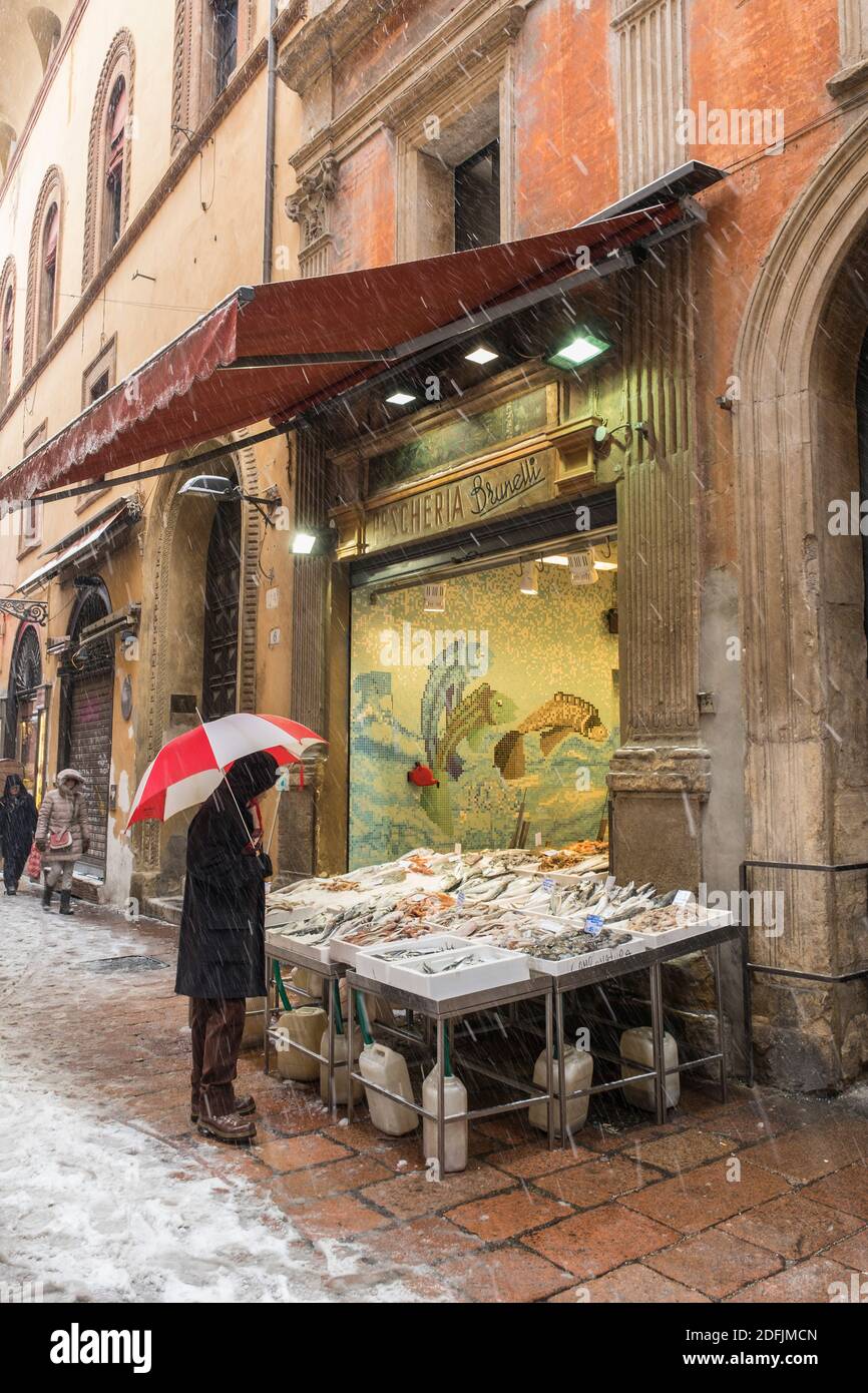 Snow falling in the historic centre of Bologna, Italy. Via delle Drapperie. Person under an
