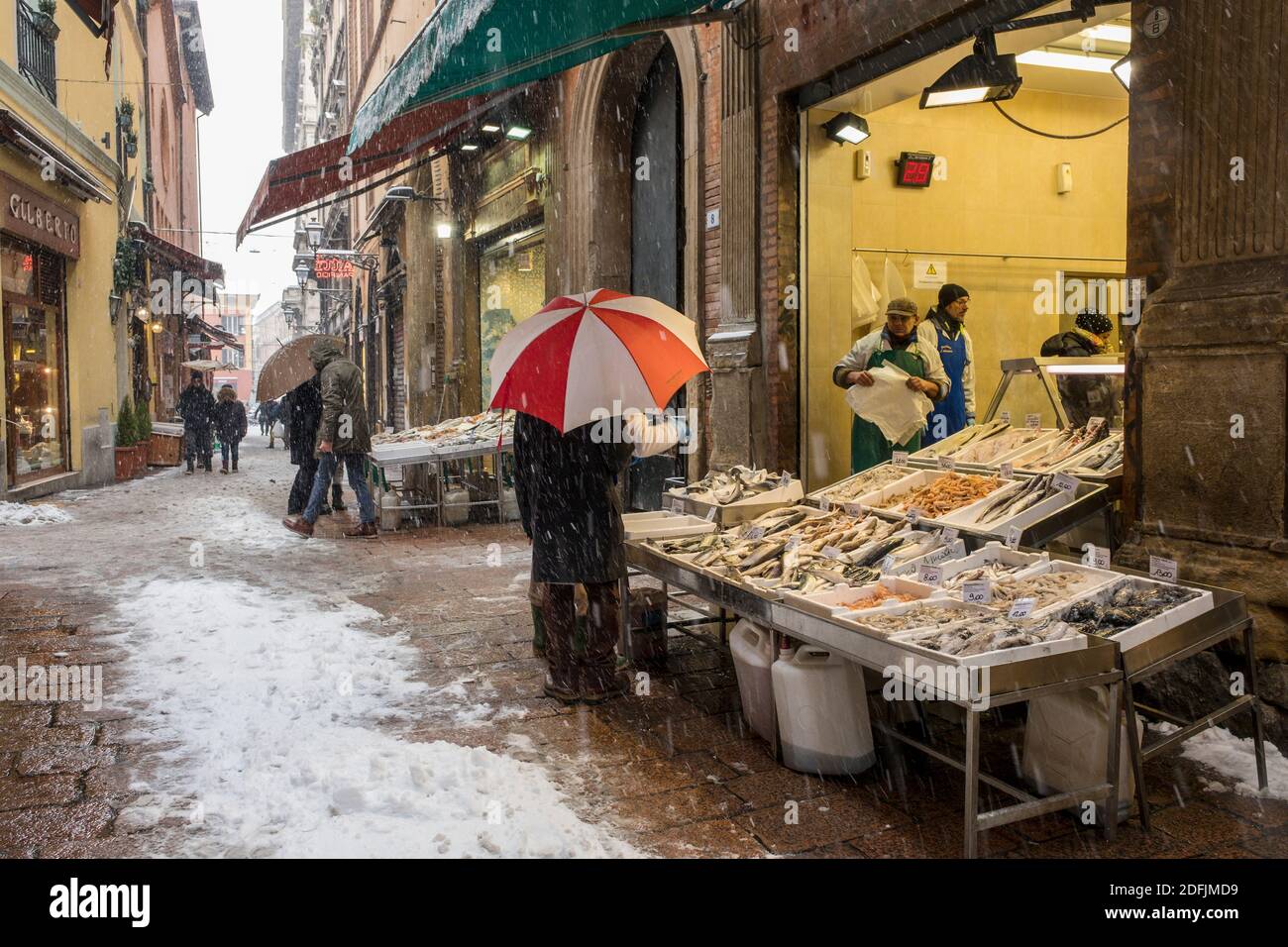 Snow falling in the historic centre of Bologna, Italy. Via delle Drapperie. Person under an