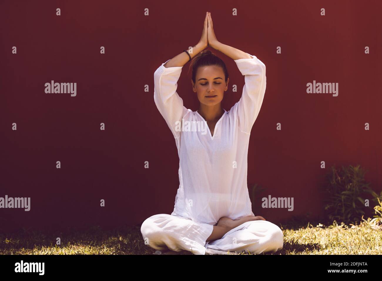 Pretty Woman Dressed in Clean White Clothes Sitting in Lotus Posture with Closed Eyes and Meditating. Inner Peace Stock Photo