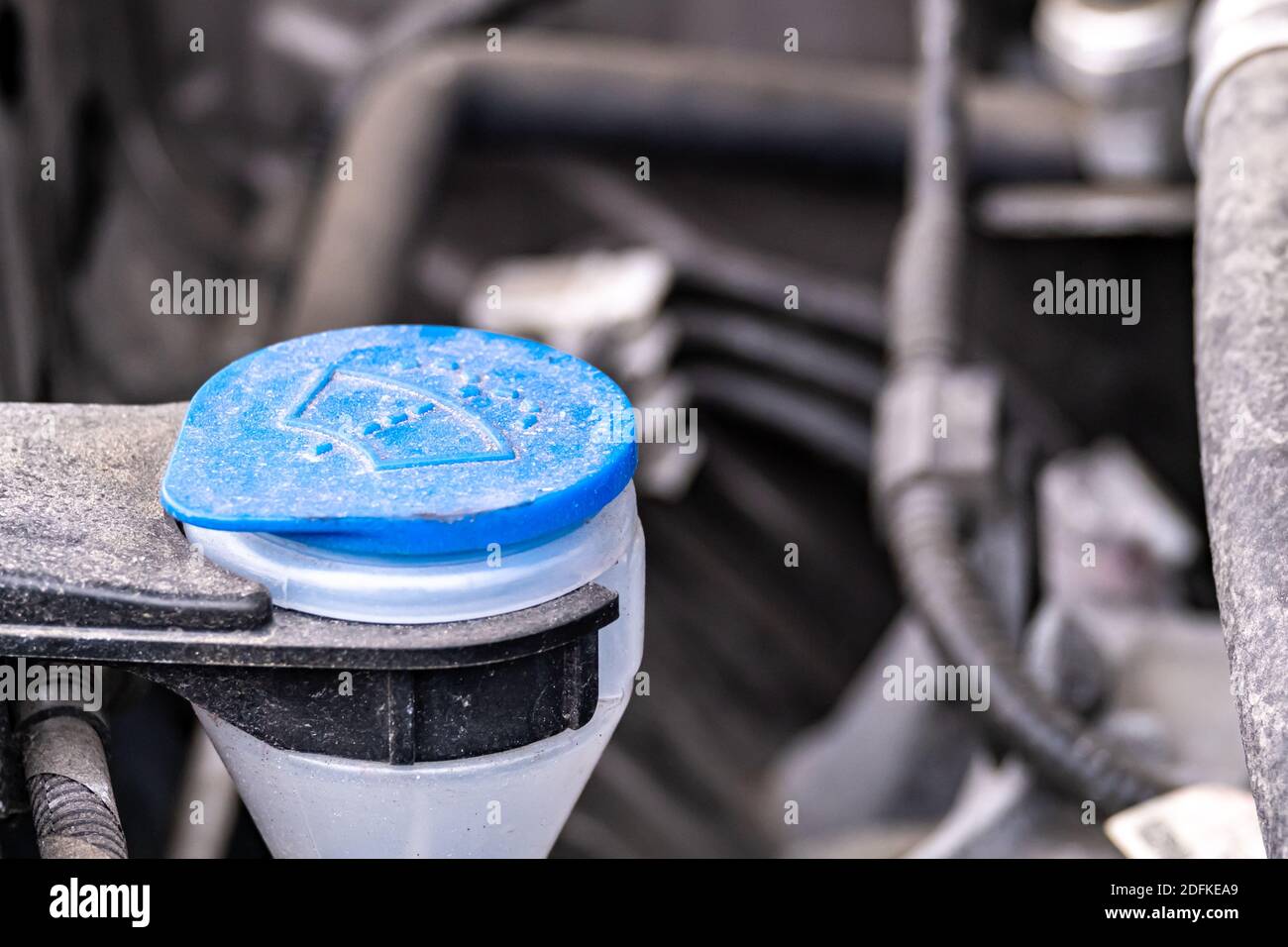 A close-up side view of a blue plastic cap covering a tube for filling a windshield wiper fluid tank. Stock Photo