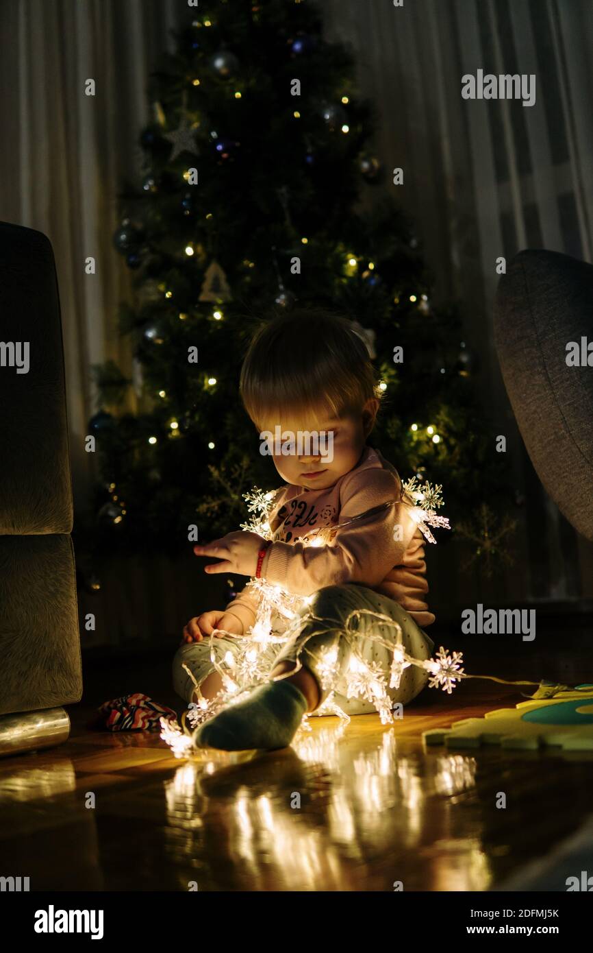 Baby girl in front of Christmas tree with Christmas light on her Stock Photo