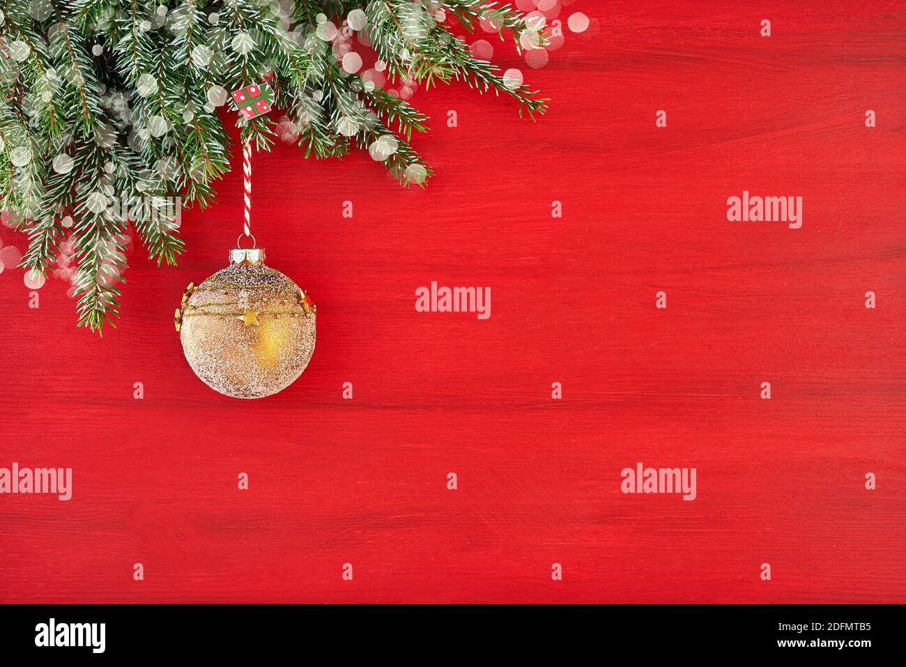 Christmas greeting card. Fir tree branch with yellow decoration. Red Christmas background. Copy space, snow texture. Stock Photo