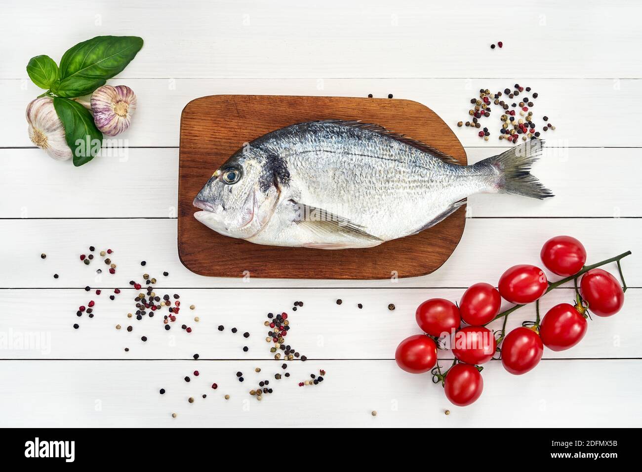 Fresh dorado fish on wooden cutting board with garlic, tomatoes and peppercorns. Top view, copy space Stock Photo