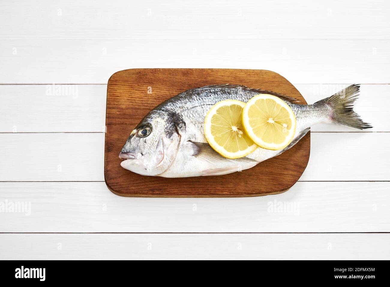 Fresh dorado fish with lemon on wooden cutting board on white wooden table. Top view, copy space Stock Photo