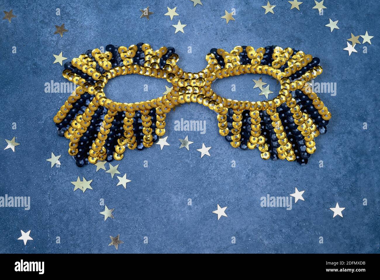 Golden glittering mask with golden stars on a blue background. Top view, copy space. Carnival party celebration concept. Stock Photo