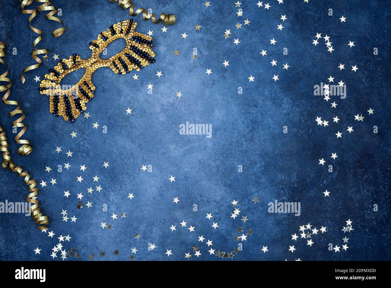 Golden glittering mask and party streamers with golden stars on a blue background. Top view, copy space. Carnival party celebration concept. Stock Photo