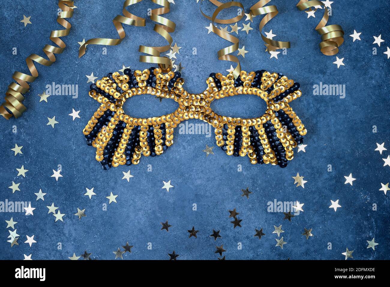 Golden glittering mask and serpentine with golden stars on a blue background. Top view, copy space. Carnival party celebration concept. Stock Photo