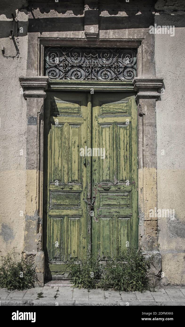 Old door in Cyprus with peeling green paint and overgrown by weeds so unused Stock Photo