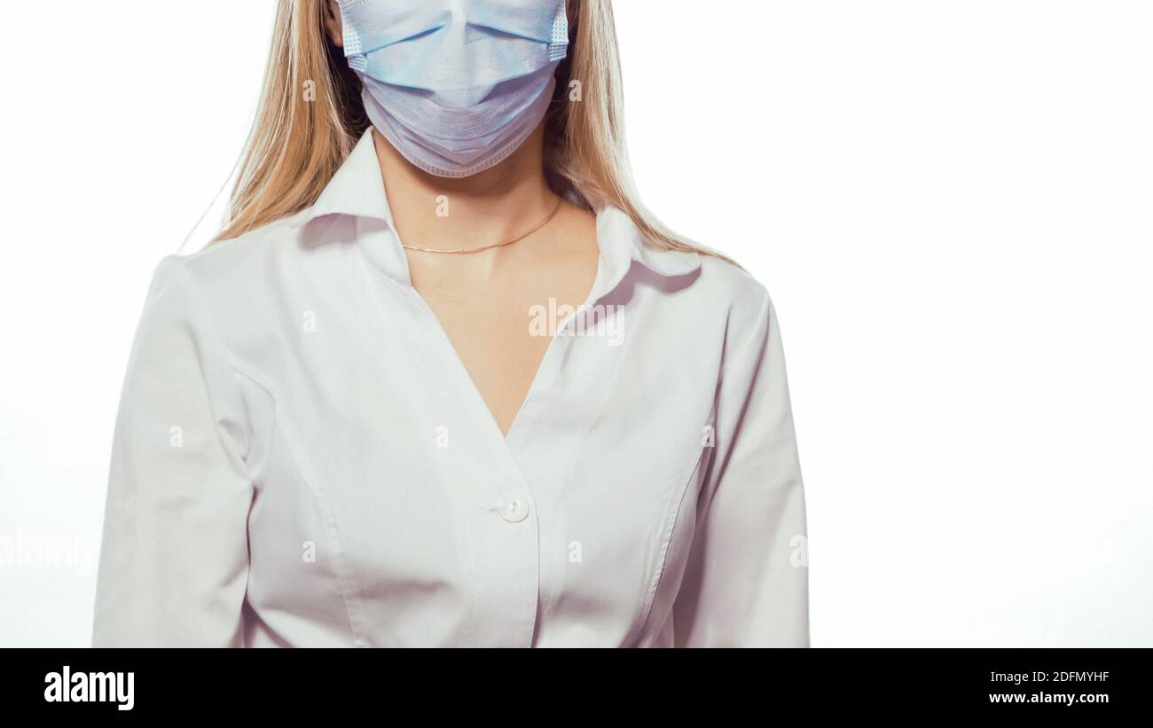 Close up, no face. Nurse in a medical mask and white uniform with blond loose hair looking at the camera. Isolated on white background Stock Photo