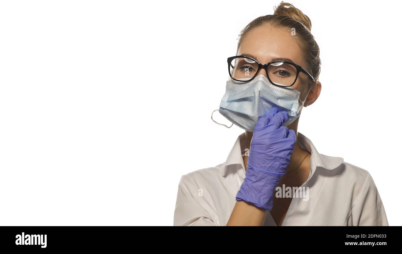 Fixing face medical mask young blond nurse in eye glasses looking at the camera wearing white medical uniform isolated on white background Stock Photo