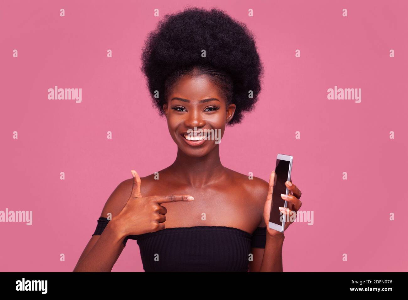 Call me. Cheerful African American young girl pointing finger at phone saying call me with gorgeous afro hairstyle standing smiling in black shoulder Stock Photo