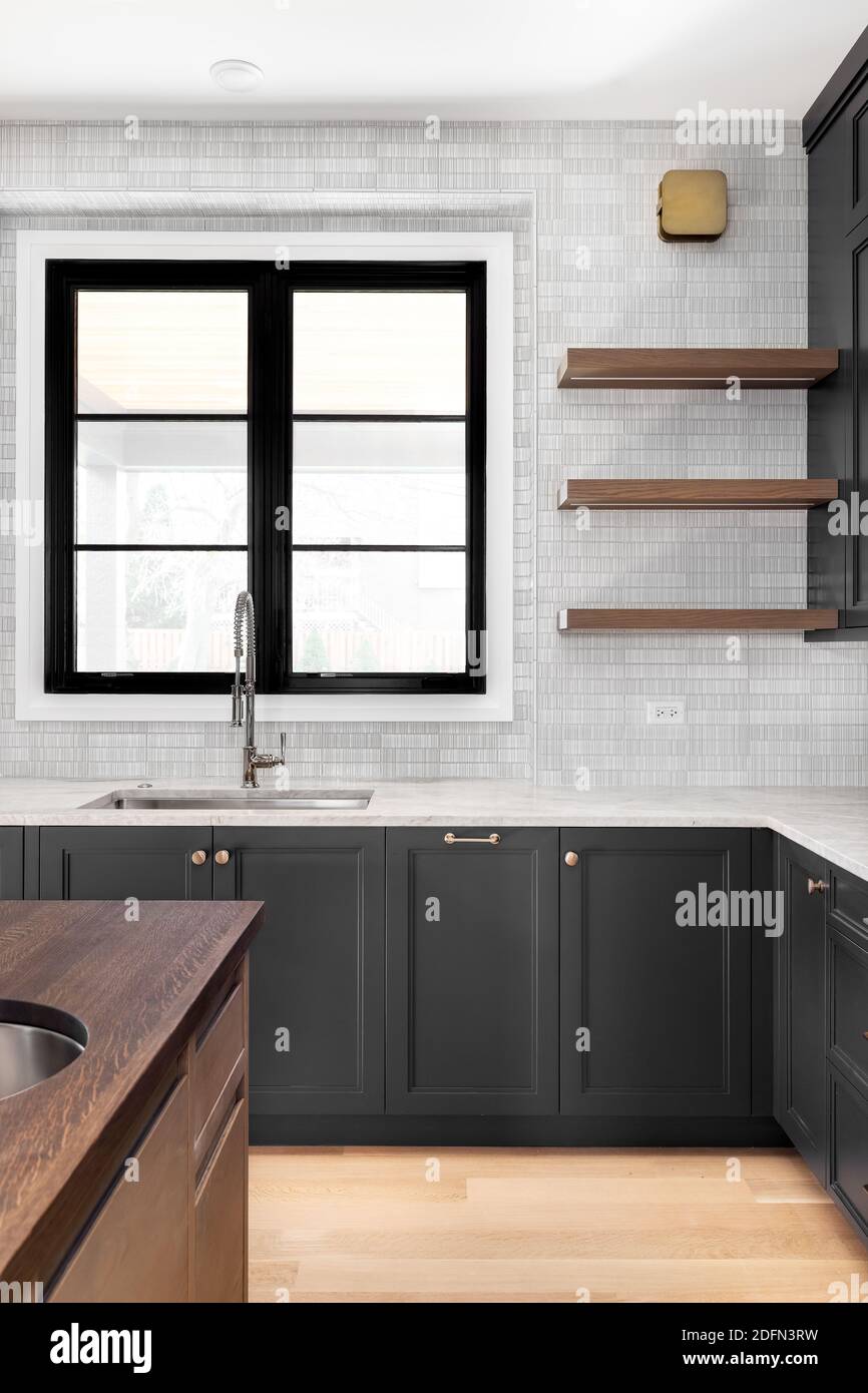 A modern kitchen with charcoal custom cabinets, a marble back splash tile,  and kitchen sink with a chrome faucet in front of a large window Stock  Photo - Alamy