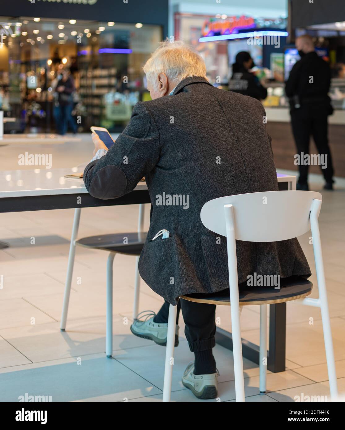 Back view of an old man 70-75 years sitting in a cafeteria and using his smartphone. Side view, street view. Stock Photo
