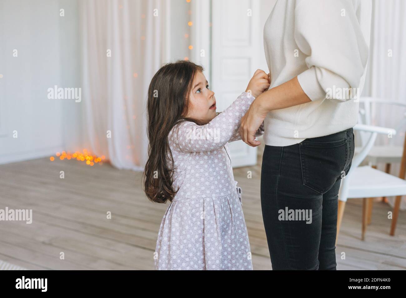 Cute long hair little girl helps dress her mother at bright bed room Stock Photo