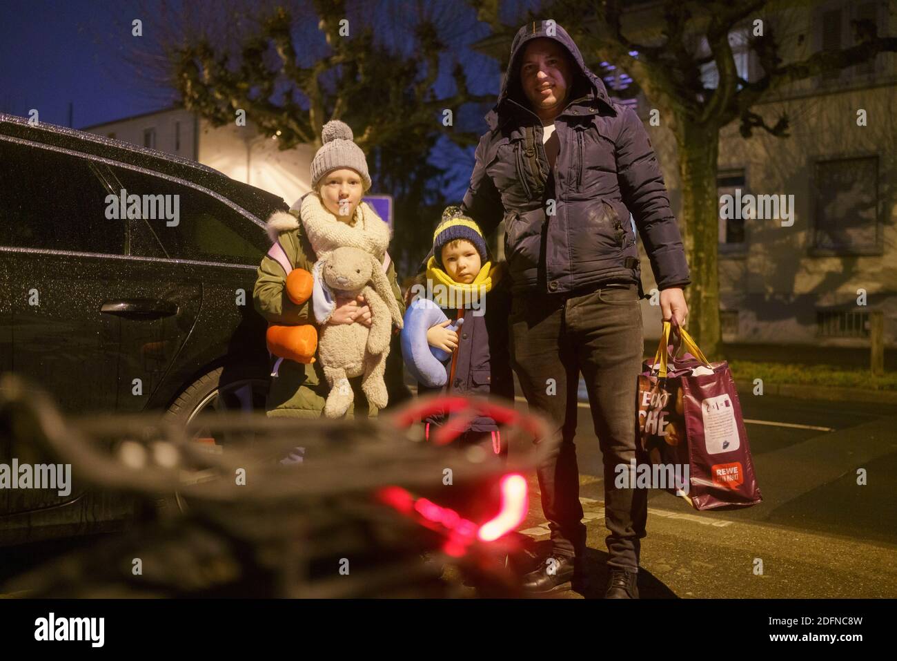 06 December 2020, Hessen, Frankfurt/Main: Artur Lisovskis (r) and his two children Alisa (l) and Artemis (M) get into their car early in the morning to leave their residential area in the Gallus district after a 500 kilogram World War II bomb was found on a nearby construction site on 3 December 2020. This is to be defused in the course of the day. Due to the amount of explosives and the design of the British type bomb, a large evacuation radius is required. Photo: Frank Rumpenhorst/dpa Stock Photo