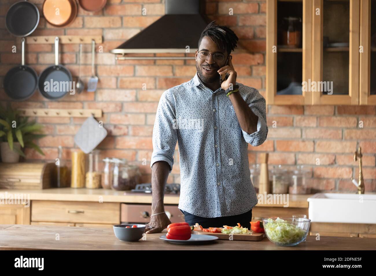 Smiling young mixed race man answering phone call, preparing food. Stock Photo