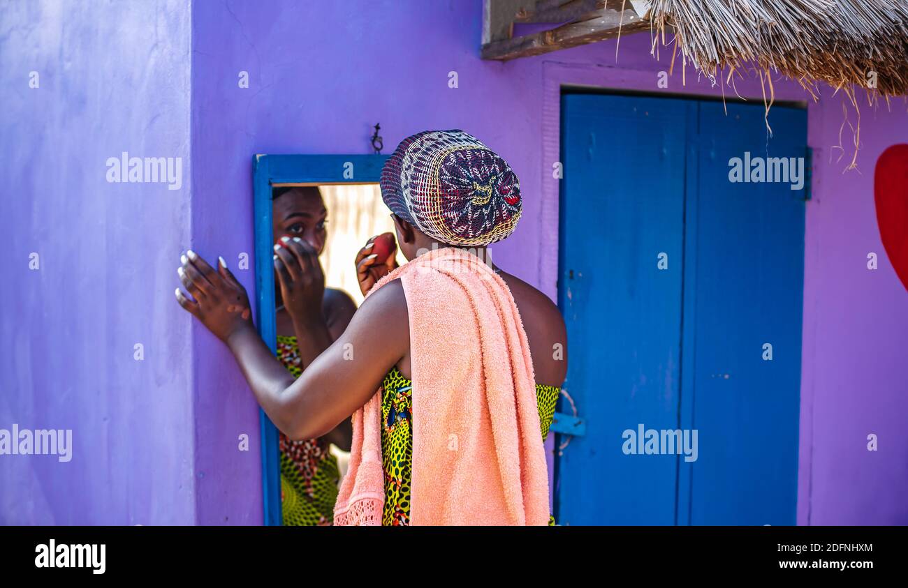 African woman doing her makeup outdoors in front of a mirror in the tropical part of Ghana West Africa Stock Photo