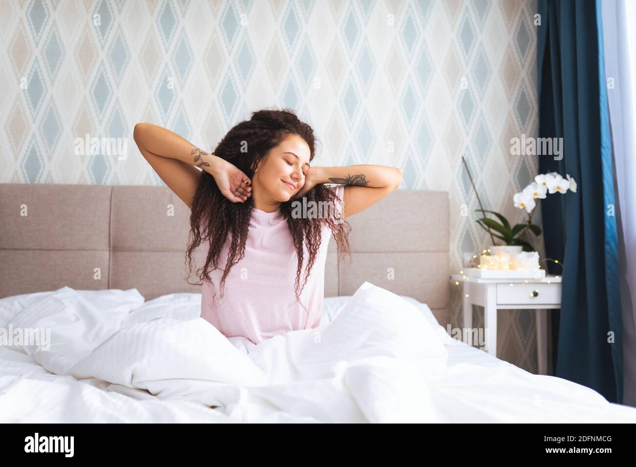 Font view of young woman waking up in early morning sitting on bed with whitesnow linen and sretch her arms and body with smile Stock Photo