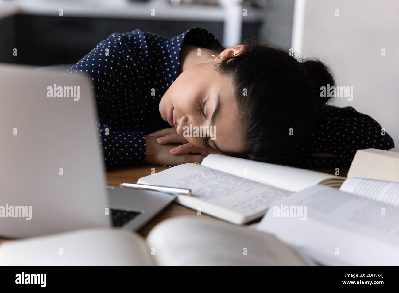 Fatigued young mixed race woman sleeping at workplace among books Stock Photo