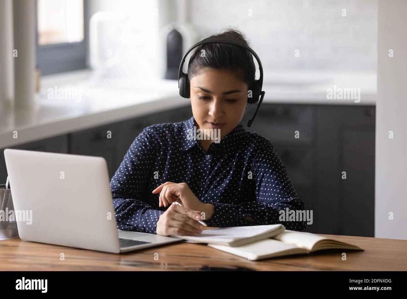 Indian female sitting by laptop wearing headphones getting education online Stock Photo