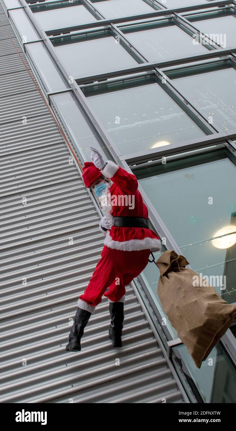 06 December 2020, Baden-W·ºrttemberg, Ulm: Christian Hagg, dressed as Santa Claus, abseils down the facade of the child and youth psychiatric clinic of the Ulm University Hospital. The height rescue team of the Ulm fire brigade abseiled Santa Claus from a height of 20 metres. The man dressed as Santa Claus brings presents for the children and young people. Photo: Stefan Puchner/dpa Stock Photo