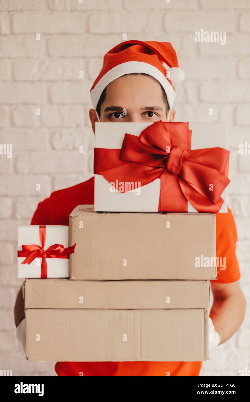 https://c8.alamy.com/comp/2DFP1GC/funny-young-man-courier-in-santa-hat-medical-face-mask-protective-gloves-deliver-christmas-new-year-gifts-happy-delivery-man-carry-cardboard-presen-2DFP1GC.jpg